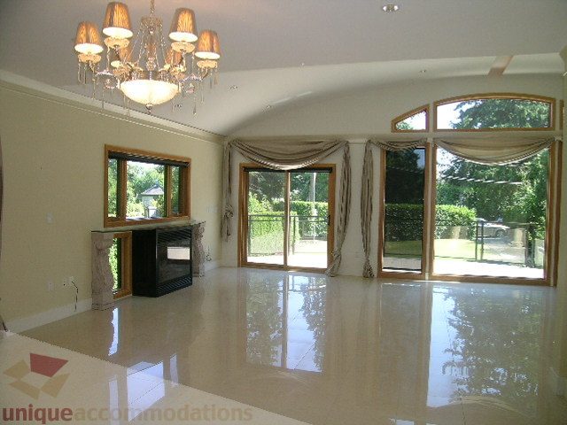 Spacious living room with glossy white floors and large windows showcasing greenery. - 4215 Evergreen Ave, West Vancouver