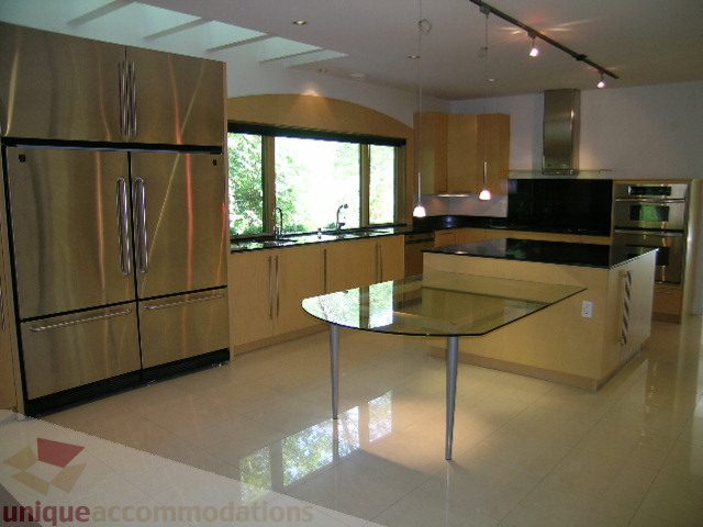 Modern kitchen with stainless steel appliances, glass dining table, and large windows. - 4215 Evergreen Ave, West Vancouver