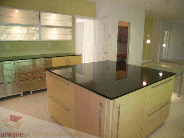 Bright kitchen with modern glass countertops and light wood cabinets. - 4215 Evergreen Ave, West Vancouver