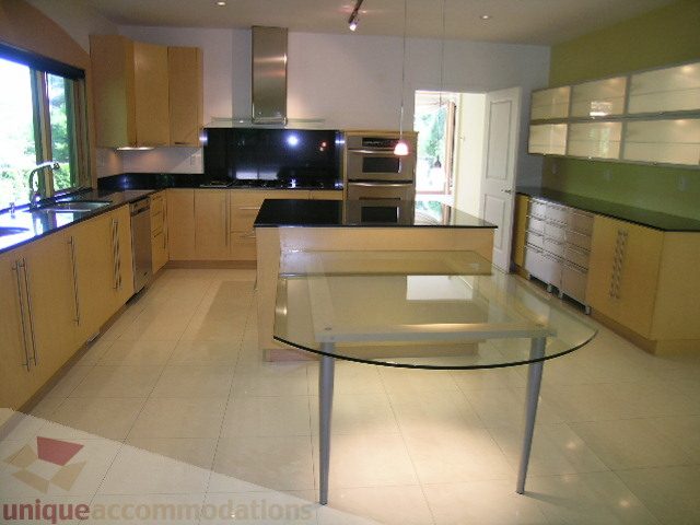 Bright kitchen with light wood cabinets, black countertops, and a large island. - 4215 Evergreen Ave, West Vancouver