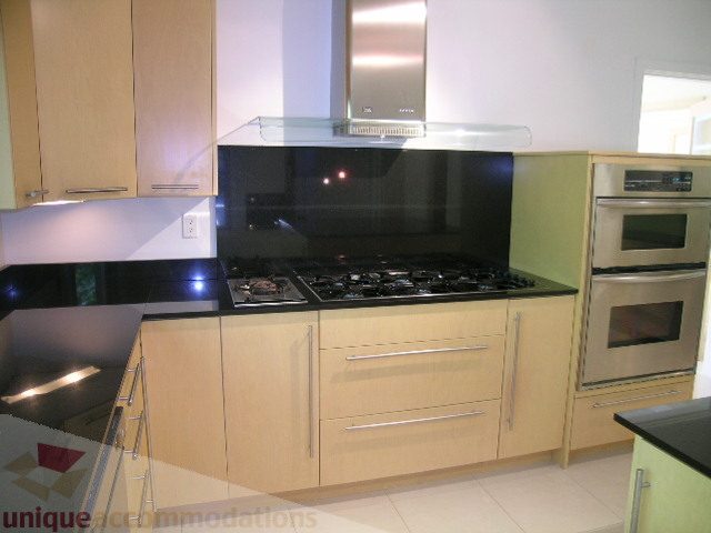 Bright kitchen with modern appliances, black countertops, and light wood cabinets. - 4215 Evergreen Ave, West Vancouver
