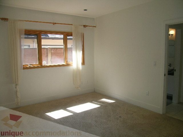 Bright bedroom with natural light, carpeted floor, and wooden window frame. - 4215 Evergreen Ave, West Vancouver
