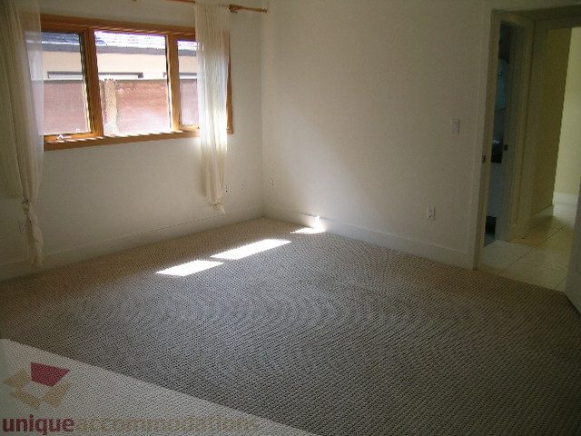 Bright bedroom with large window, neutral carpet, and open door leading to another room. - 4215 Evergreen Ave, West Vancouver