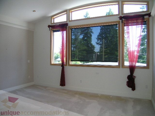 Bright living room with large windows and red curtains, showcasing a city view. - 4215 Evergreen Ave, West Vancouver