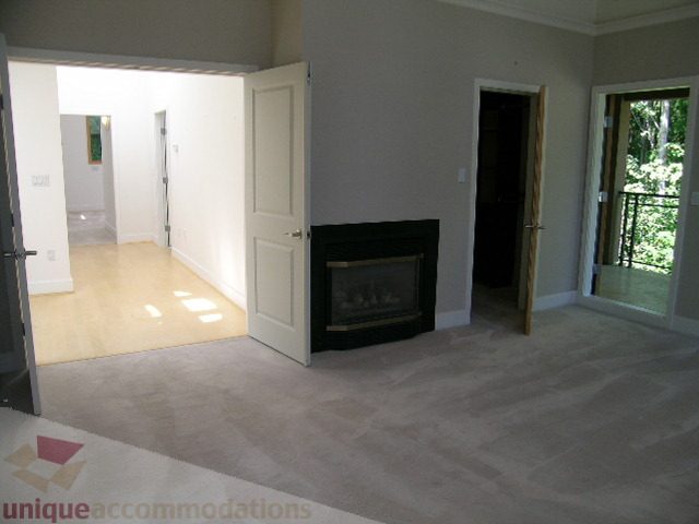 Spacious living room with hardwood floors and a fireplace, leading to a bright hallway. - 4215 Evergreen Ave, West Vancouver