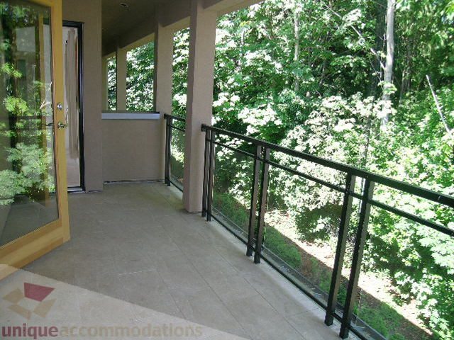Bright balcony with glass railings and lush green trees in the background. - 4215 Evergreen Ave, West Vancouver