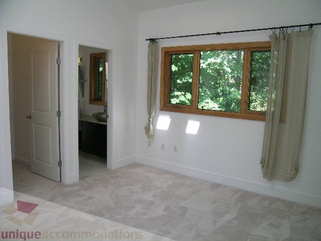 Bright bedroom with large windows and hardwood floors, leading to a bathroom. - 4215 Evergreen Ave, West Vancouver
