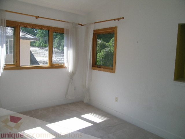Bright bedroom with large windows and light-colored walls, carpeted floor. - 4215 Evergreen Ave, West Vancouver