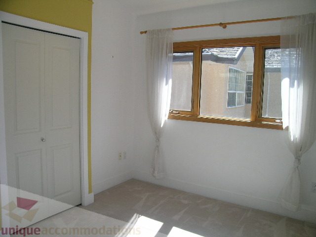 Bright bedroom with large window and sheer curtains, ready for furnishings. - 4215 Evergreen Ave, West Vancouver