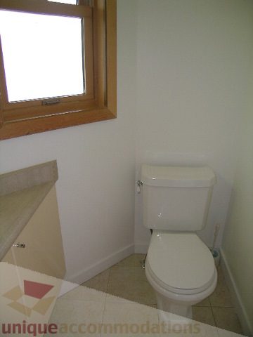 Small bathroom with white toilet and sink, natural light from window. - 4215 Evergreen Ave, West Vancouver