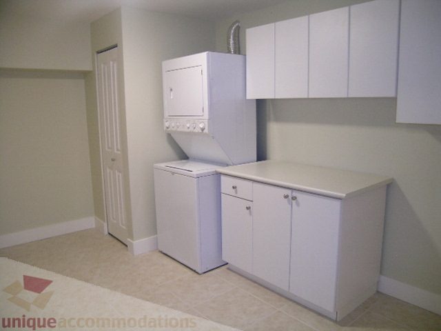 Bright laundry room with white cabinets and countertop, carpeted floor. - 4215 Evergreen Ave, West Vancouver