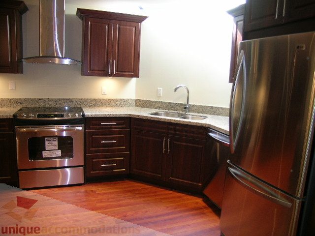 Bright kitchen with dark wood cabinets, stainless steel appliances, and granite countertops. - 4215 Evergreen Ave, West Vancouver