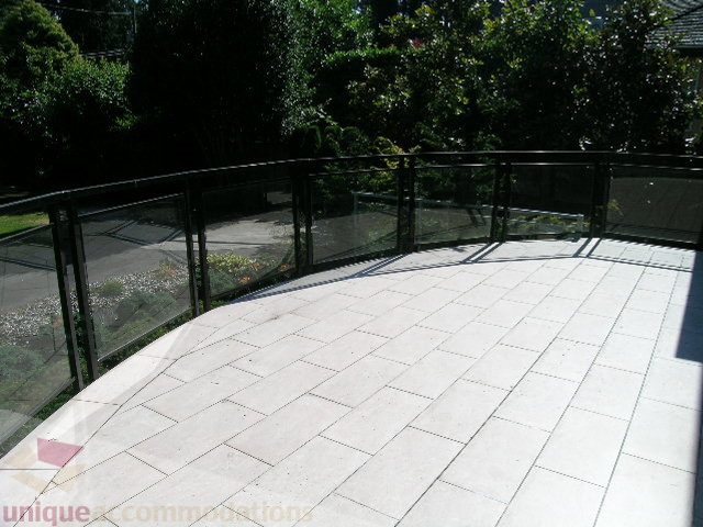 Spacious outdoor deck with glass railings and stone paving, surrounded by lush greenery. - 4215 Evergreen Ave, West Vancouver