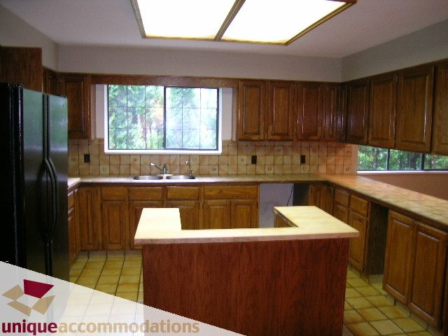 Bright kitchen with wooden cabinets, tiled countertops, and a large window. - 5568 Greenleaf Road, West Vancouver