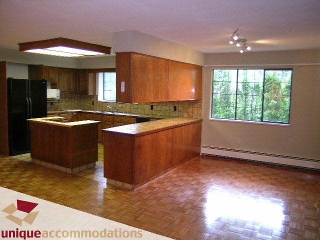 Bright kitchen with wooden cabinets, granite countertops, and hardwood floors, featuring a large window with a city view.