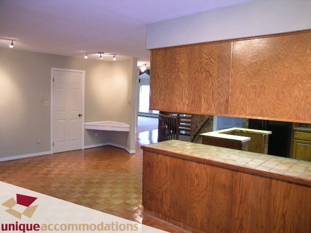 Bright kitchen with wood cabinets and tiled countertops, hardwood floors, and a view of the living area. - 5568 Greenleaf Road, West Vancouver