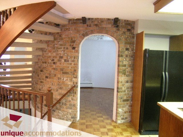Framed brick archway leading to a cozy living area with hardwood floors and a modern kitchen in the background. - 5568 Greenleaf Road, West Vancouver