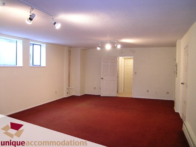 Spacious living room with red carpet and white walls, featuring a door leading to another room. - 5568 Greenleaf Road, West Vancouver
