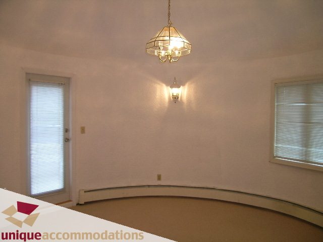 Bright living room with curved wall and chandelier. - 5568 Greenleaf Road, West Vancouver