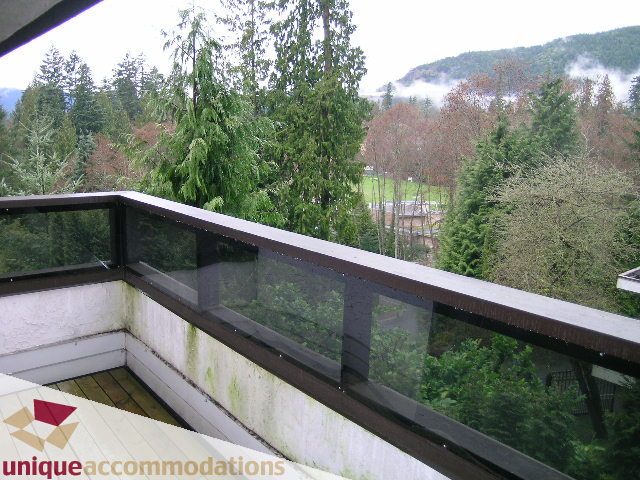 Balcony with glass railing, overlooking lush green trees and misty mountains. - 5568 Greenleaf Road, West Vancouver
