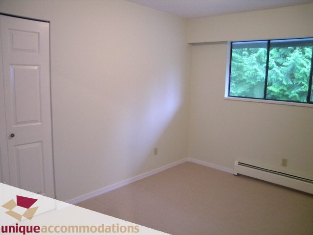 Bright bedroom with carpeted floor and large window showing greenery. - 5568 Greenleaf Road, West Vancouver