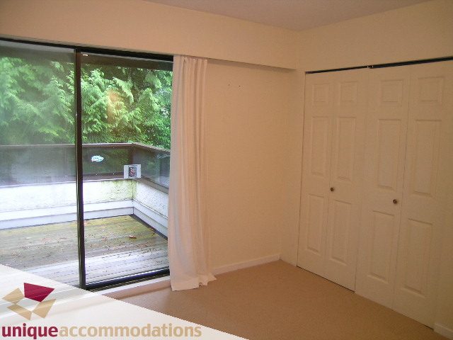 Bright bedroom with sliding glass door, hardwood floors, and a view of greenery outside. - 5568 Greenleaf Road, West Vancouver