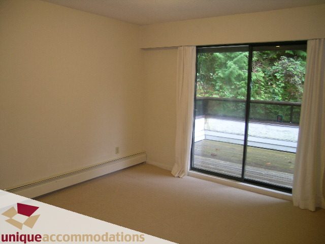 Spacious living room with large sliding glass doors, greenery view, and neutral carpet. - 5568 Greenleaf Road, West Vancouver