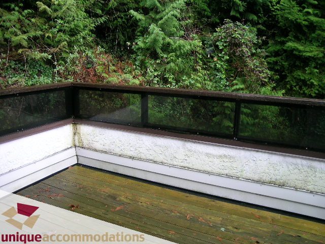 Furnished balcony with wooden deck and glass railing, surrounded by lush greenery. - 5568 Greenleaf Road, West Vancouver