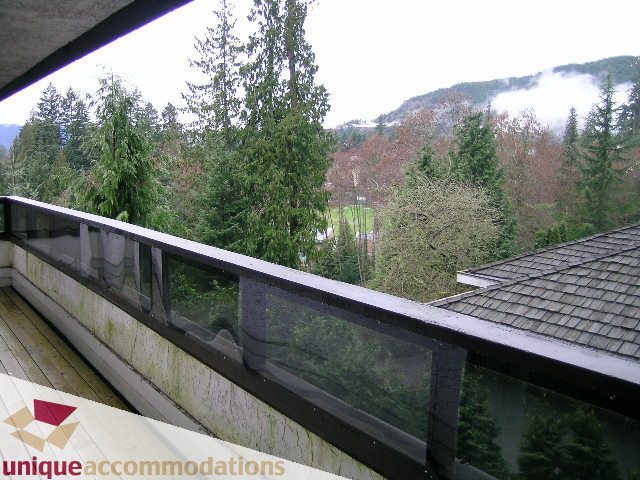 Balcony with glass railings and a view of evergreen trees and mountains. - 5568 Greenleaf Road, West Vancouver