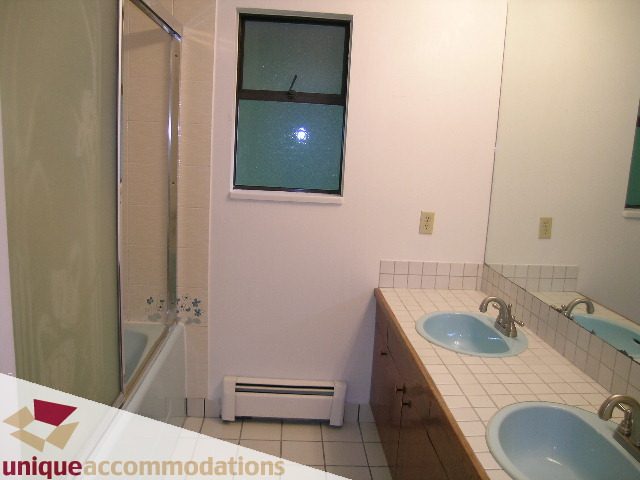 Bright bathroom with white countertop and dual sinks, modern shower, and window view. - 5568 Greenleaf Road, West Vancouver