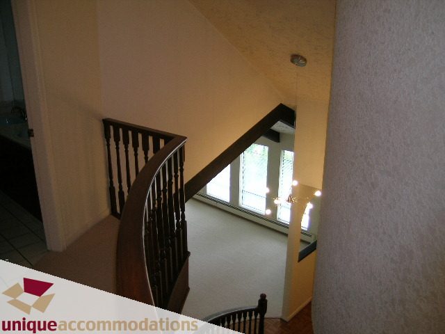 Staircase leading to upper level with wooden banister and natural light. - 5568 Greenleaf Road, West Vancouver