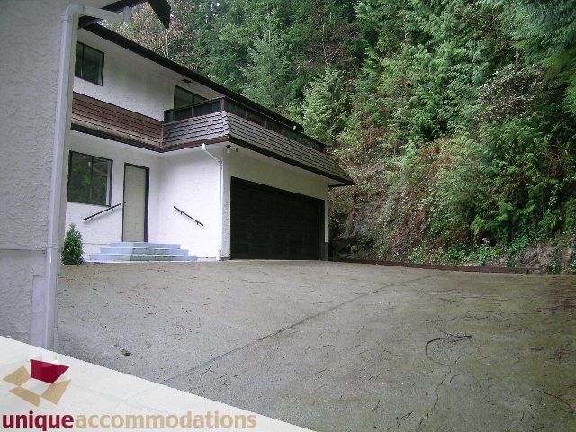 Spacious living room with large windows and a balcony, surrounded by lush greenery. - 5568 Greenleaf Road, West Vancouver