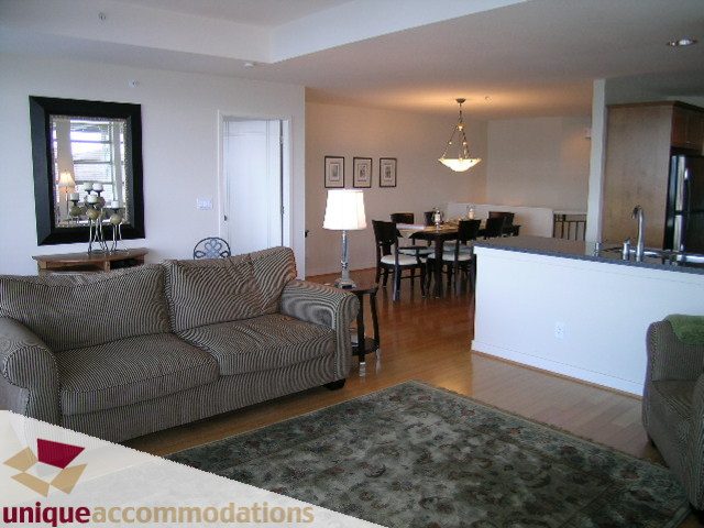 Open-concept living room with striped sofas, hardwood floors, and a dining area in the background. - 8583 Seascape Lane, West Vancouver