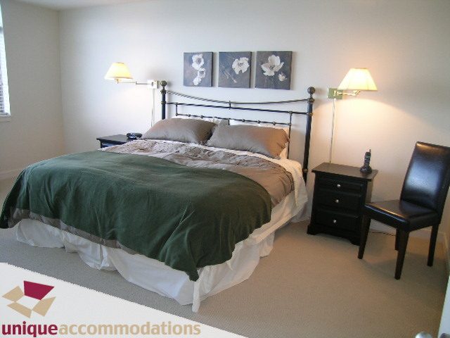 Spacious bedroom with a large bed, green bedding, and a nightstand with a lamp. - 8583 Seascape Lane, West Vancouver