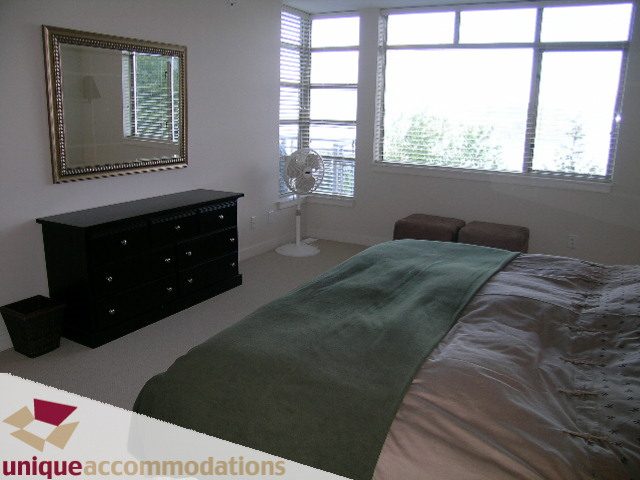 Spacious bedroom with large windows, green bedding, and a black dresser. - 8583 Seascape Lane, West Vancouver