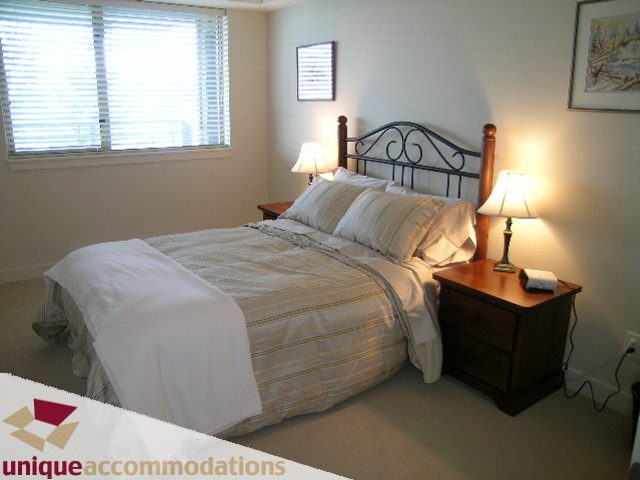 Spacious bedroom with a cozy bed, wooden nightstands, and warm lighting. - 8583 Seascape Lane, West Vancouver