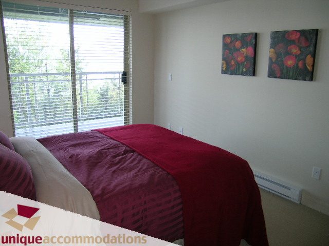 Spacious bedroom with red bedding, large window with blinds, and floral wall art. - 8583 Seascape Lane, West Vancouver