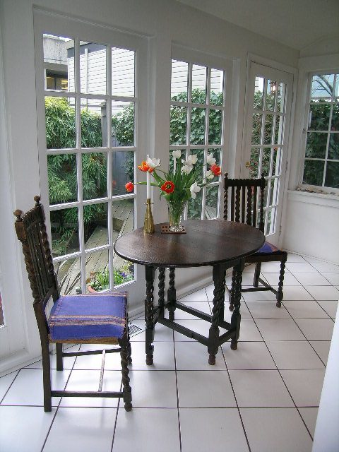 Bright sunroom with tiled floor, wooden furniture, and large windows overlooking greenery. - 1152 West 7th Ave, Vancouver West Side