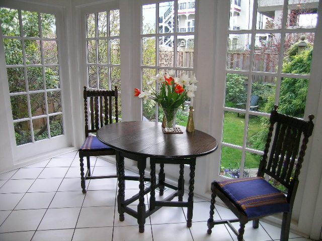 Bright sunroom with large windows, white tiled floor, and wooden chairs, offering a view of the garden. - 1152 West 7th Ave, Vancouver West Side