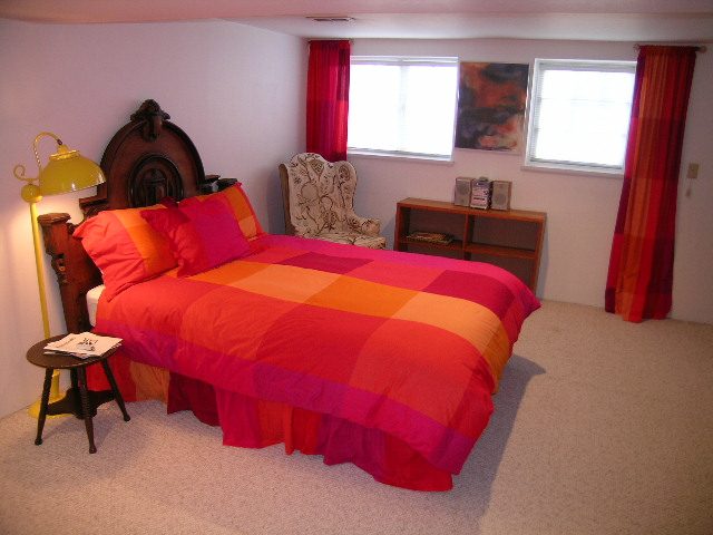 Bright bedroom with vibrant pink and orange bedding, wooden furniture, and red curtains. - 1152 West 7th Ave, Vancouver West Side