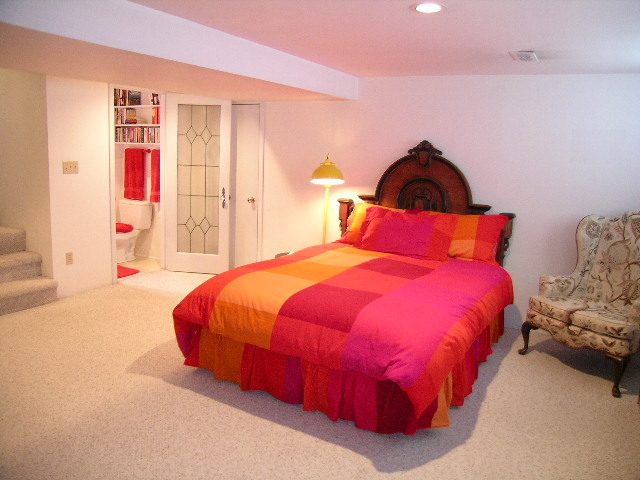Bright bedroom with colorful bedding and floral armchair, carpeted floor. - 1152 West 7th Ave, Vancouver West Side