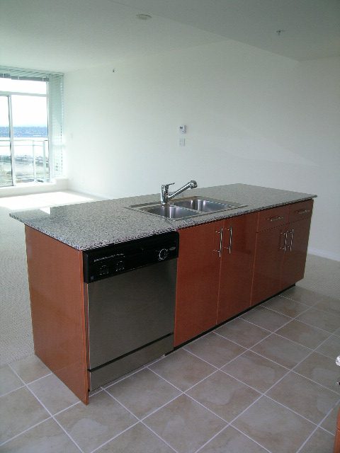 Modern kitchen with granite countertops and stainless steel appliances, featuring a city view. - 1801 - 188 East Esplanade, North Vancouver