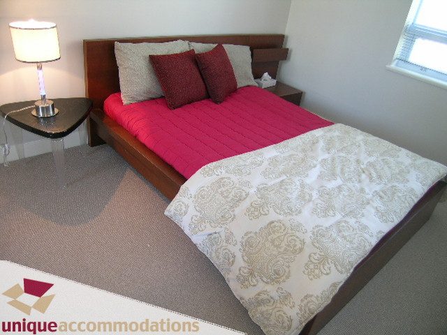 Furnished bedroom with a wooden bed, red bedding, and patterned throw blanket. - 1905 - 638 Beach Cres, Vancouver Downtown