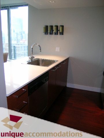 Bright kitchen with modern stainless steel sink, white countertops, dark wood cabinets, hardwood floors, and city view.