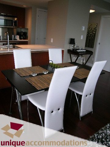 Modern dining area with sleek black table, white chairs, and wooden placemats. - 3104 - 1255 Seymour Street, Vancouver Downtown