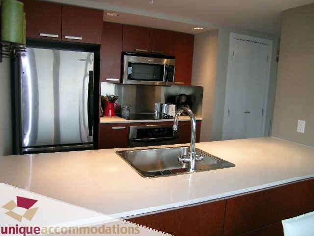 Bright kitchen with modern stainless steel appliances, granite countertops, and dark wood cabinets. - 3104 - 1255 Seymour Street, Vancouver Downtown