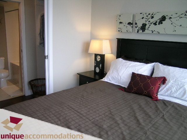 Furnished bedroom with dark headboard, white bedding, and red accent pillows. - 3104 - 1255 Seymour Street, Vancouver Downtown