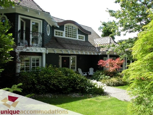 Spacious 7-bedroom house with a charming black and white exterior, surrounded by lush greenery and a well-maintained lawn.