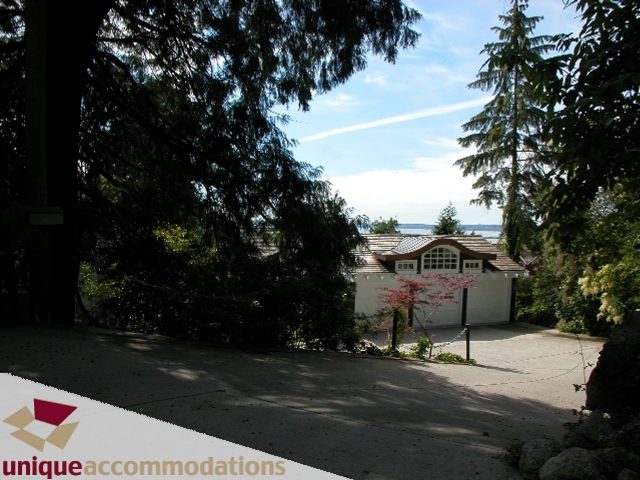 Spacious 7-bedroom house with a serene, tree-lined driveway and a distant city view. - 3586 Creery Ave, West Vancouver