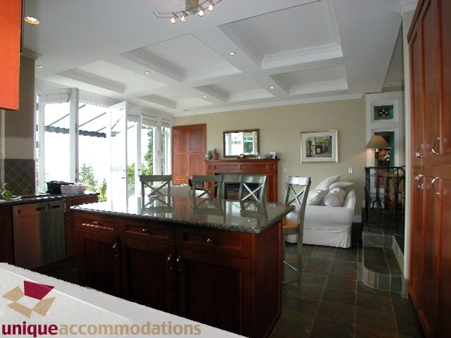 Modern kitchen with granite countertops, hardwood floors, and a cozy living area in the background. - 3586 Creery Ave, West Vancouver